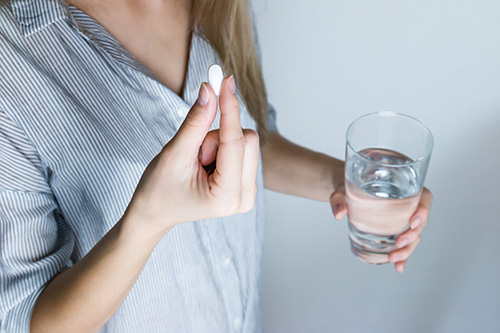 A woman holds a pill and a glass of water