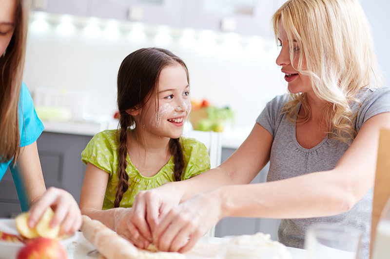 Portrait of happy girl helping her mother to cook pastry