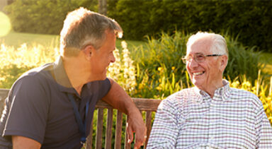 Two happy men sitting on a bench talking - the human given approach